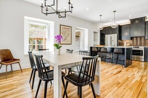 A modern kitchen with a central island, black chairs, and a wooden dining table. - Historic Home a Block From Main St With Hot Tub, Sauna, Fast Wifi & Firepit (Fredericksburg)