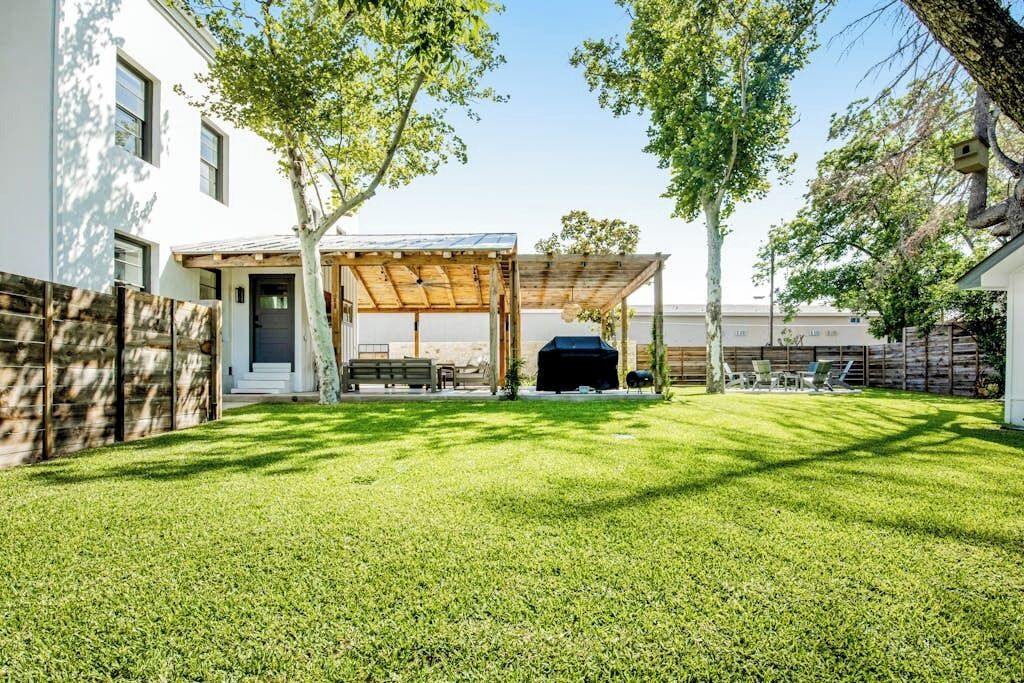 Ein Garten mit überdachter Terrasse, Grill und gepflegtem Rasen.