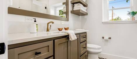 Un baño con lavamanos blanco, un espejo, un inodoro y una ventana que da a vistas exteriores.