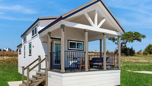 A single-story house with a covered porch, a staircase leading to the entrance, and a view of the surrounding landscape. - Modern Tiny Home With Loft, Kitchen, Cozy Patio and Shared Pools, Great Location (Fredericksburg)