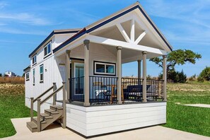 A single-story house with a covered porch, a staircase leading to the entrance, and a view of the surrounding landscape. - Modern Tiny Home With Loft, Kitchen, Cozy Patio and Shared Pools, Great Location (Fredericksburg)