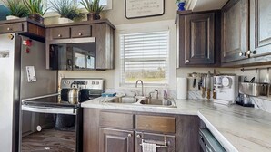 A kitchen with dark wood cabinets, a stainless steel sink, a built-in oven, and a window with blinds. - Modern Tiny Home With Loft, Kitchen, Cozy Patio and Shared Pools, Great Location (Fredericksburg)