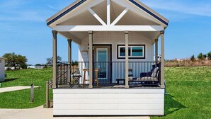 A small, single-story house with a porch, a door, and a window. - Modern Tiny Home With Loft, Kitchen, Cozy Patio and Shared Pools, Great Location (Fredericksburg)