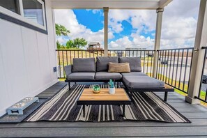 A balcony with a grey sectional sofa, a wooden coffee table, and a striped rug. - Modern Tiny Home With Loft, Kitchen, Cozy Patio and Shared Pools, Great Location (Fredericksburg)