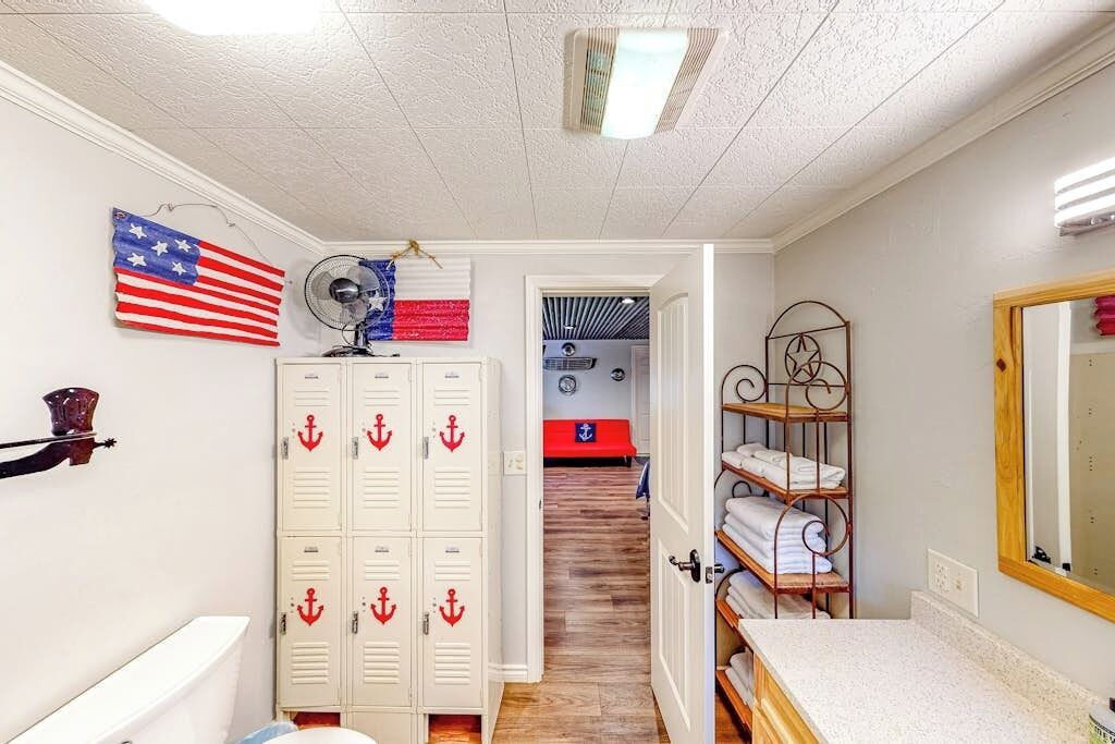A room with lockers, a fan, a mirror, and a view into another room.