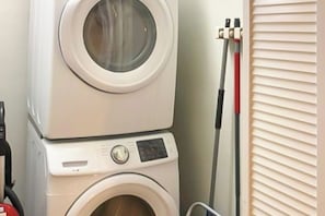 A stacked washer and dryer unit, a hose reel, and a window with blinds. - Charming Dog-friendly Lakefront Home With Lake View, Dock, & Washer/dryer (Kingsland)