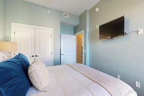 A bedroom with a bed, a TV mounted on the wall, and a door leading to another room. - Hill Country Corner Condo at The Waters - Central AC, Lake Views & Pool (Horseshoe Bay)
