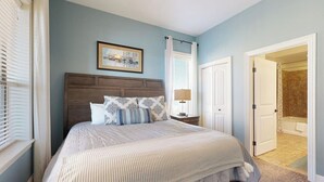 Une chambre à coucher comprenant un lit, une table de chevet, une lampe, un tableau encadré et une porte donnant sur une salle de bain.