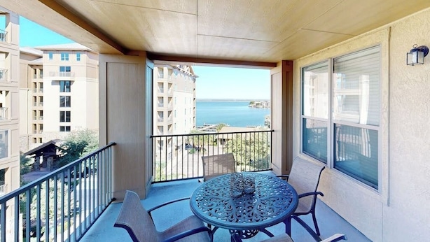 Un balcon avec une table et des chaises, une vue sur l’océan et les bâtiments avoisinants.