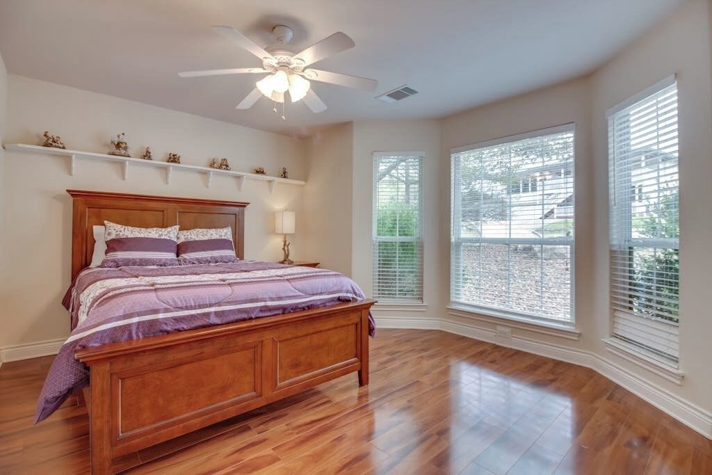 Une chambre avec un lit en bois, un ventilateur de plafond, de grandes fenêtres et un plafond blanc.