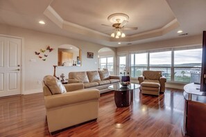 A spacious living room with a large window, a ceiling fan, and a view of the outdoors. - Wonderful Lake-view Home With Game Room & Firepit (Leander)