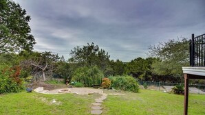 Un cortile con vialetto in pietra, recinzione e diverse piante e arbusti.