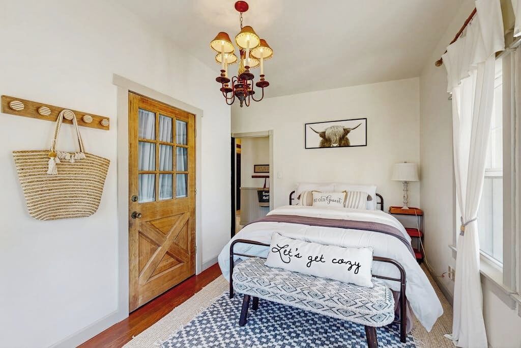 Une chambre à coucher avec un lit, un lustre, une porte en bois, un panier fixé au mur et un tableau encadré.