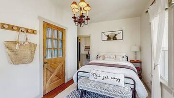Une chambre à coucher avec un lit, un lustre, une porte en bois, un panier fixé au mur et un tableau encadré.