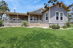 A two-story house with a porch, a small attached garage, and a well-maintained lawn. - Cozy Ranch Home With Full Kitchen, Living Room, Hot Tub, Pet-friendly & Fireplace (Fredericksburg)