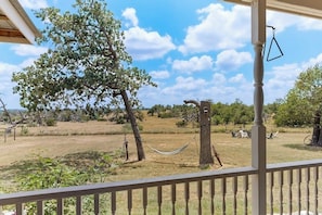 A balcony with a view of a grassy field, a hammock, and a tree. - Cozy Ranch Home With Full Kitchen, Living Room, Hot Tub, Pet-friendly & Fireplace (Fredericksburg)