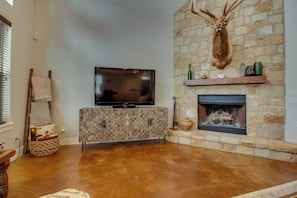 A living room with a stone fireplace, a mounted deer head, a flat-screen TV, and a woven basket.