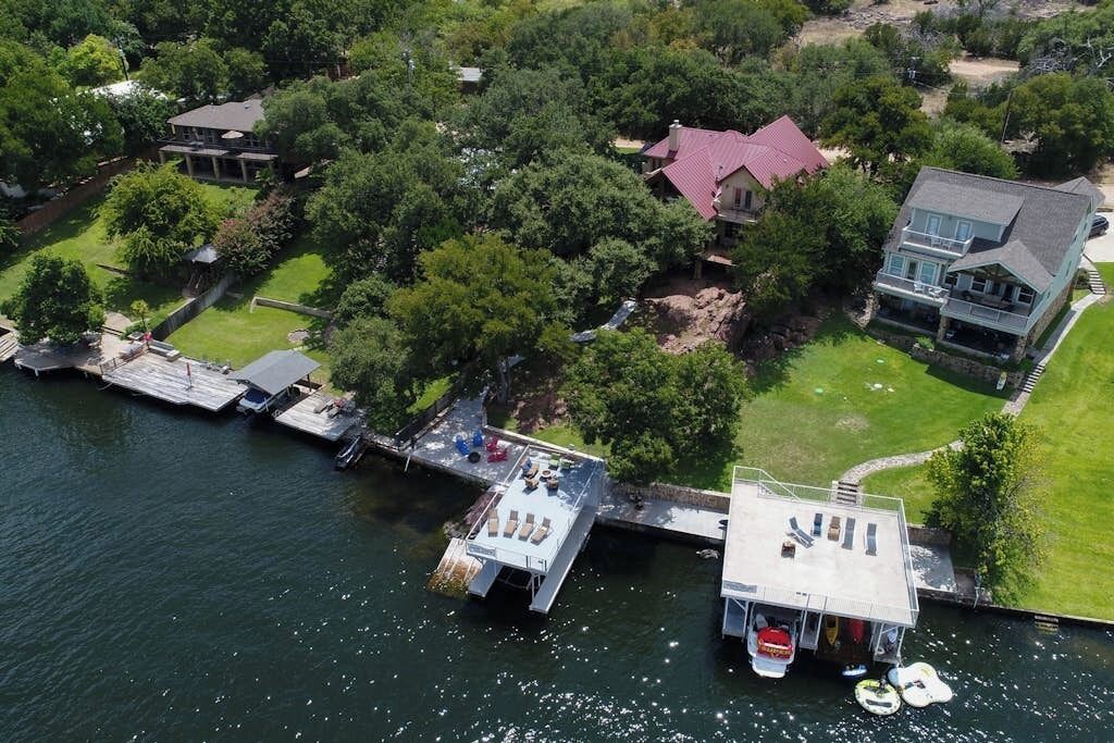An aerial view of a lakeside property with a dock, a house with a red roof, and a boat.