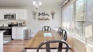 Ein Essbereich mit Holztisch, Stühlen, einer Chandelüster und einer Küche im Hintergrund.