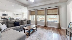 Ein geräumiges Wohnzimmer mit einer grauen Eckcouch, einem Holztisch und einem Deckenventilator.
