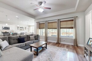 Uma sala de estar espaçosa com um sofá modular cinza, uma mesa de centro de madeira e um ventilador de teto.