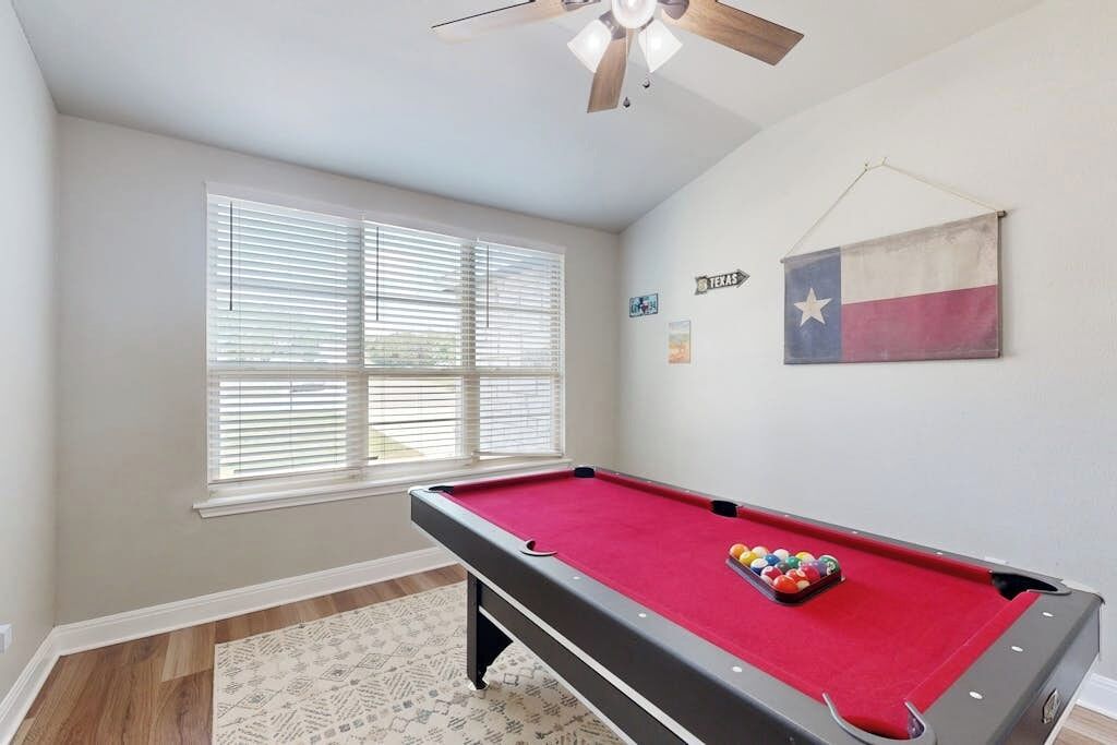 A pool table with balls, a ceiling fan, a window with blinds, and a Texas flag on the wall.