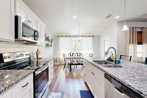 Una cocina moderna con armarios blancos, encimera de granito, horno empotrado y una zona de comedor con mesa y sillas.