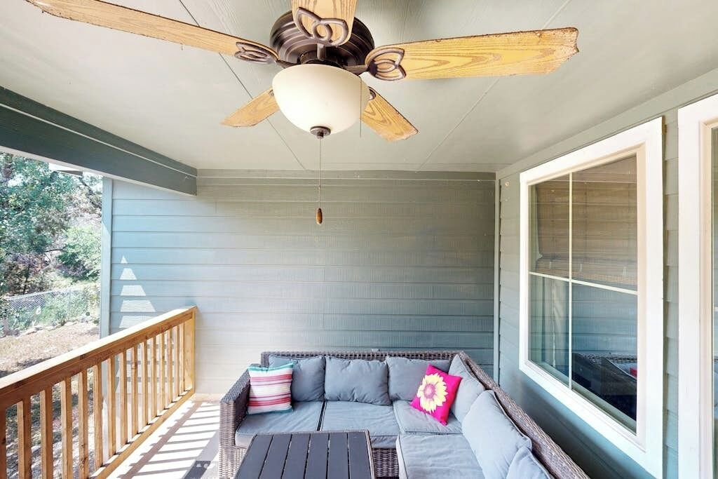 A covered porch with a ceiling fan, a gray sofa with cushions, and a wooden railing.