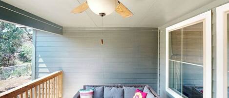 A covered porch with a ceiling fan, a gray sofa with cushions, and a wooden railing.
