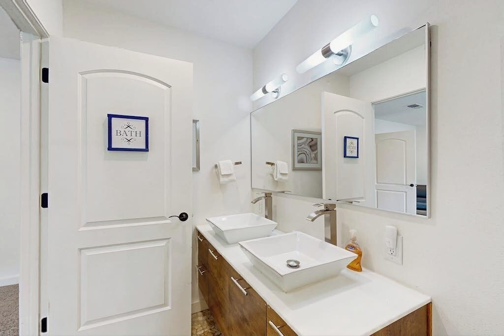 Une salle de bain avec une porte blanche, deux lavabos, un grand miroir et un tableau encadré au mur.