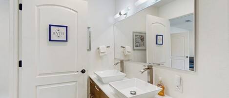 Une salle de bain avec une porte blanche, deux lavabos, un grand miroir et un tableau encadré au mur.