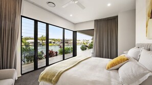 Ein Schlafzimmer mit einem großen Bett, einem Deckenventilator und Blick auf einen Pool und Gebäude.