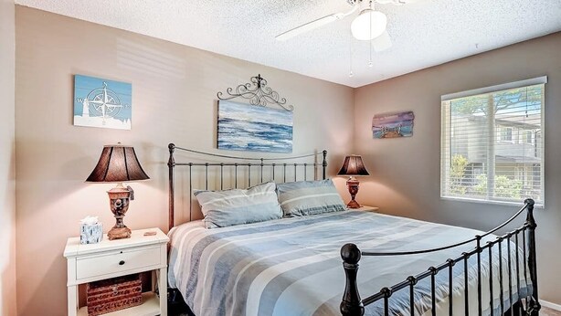 Quarto com cama, mesas de cabeceira, luminárias, ventilador de teto e obras de arte nas paredes.