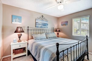 Un dormitorio con cama, mesitas de noche, lámparas, ventilador de techo y obras de arte en las paredes.