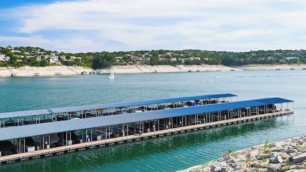 A waterfront restaurant with outdoor seating, a pier extending into the water, and a backdrop of hills and houses. - 2-story Townhouse With Balcony, Outdoor Pool, Tennis, Grill, Basketball, & AC (Leander)