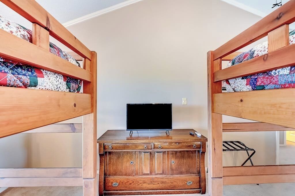 A bunk bed room with a television on a wooden dresser.