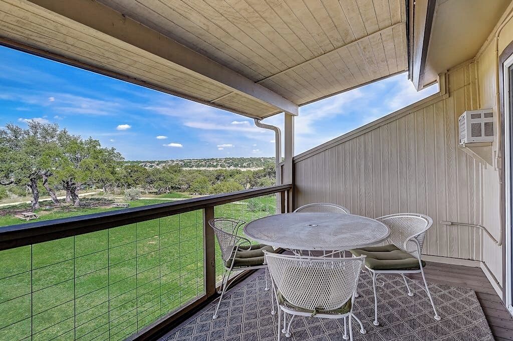 Een balkon met een tafel en stoelen, uitzicht op groen en een gebouw met een houten gevel.