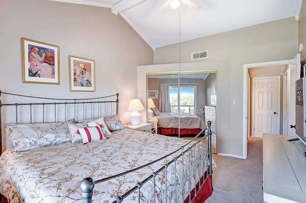 A bedroom with a bed, bedside tables, a mirror, and a door leading to another room.