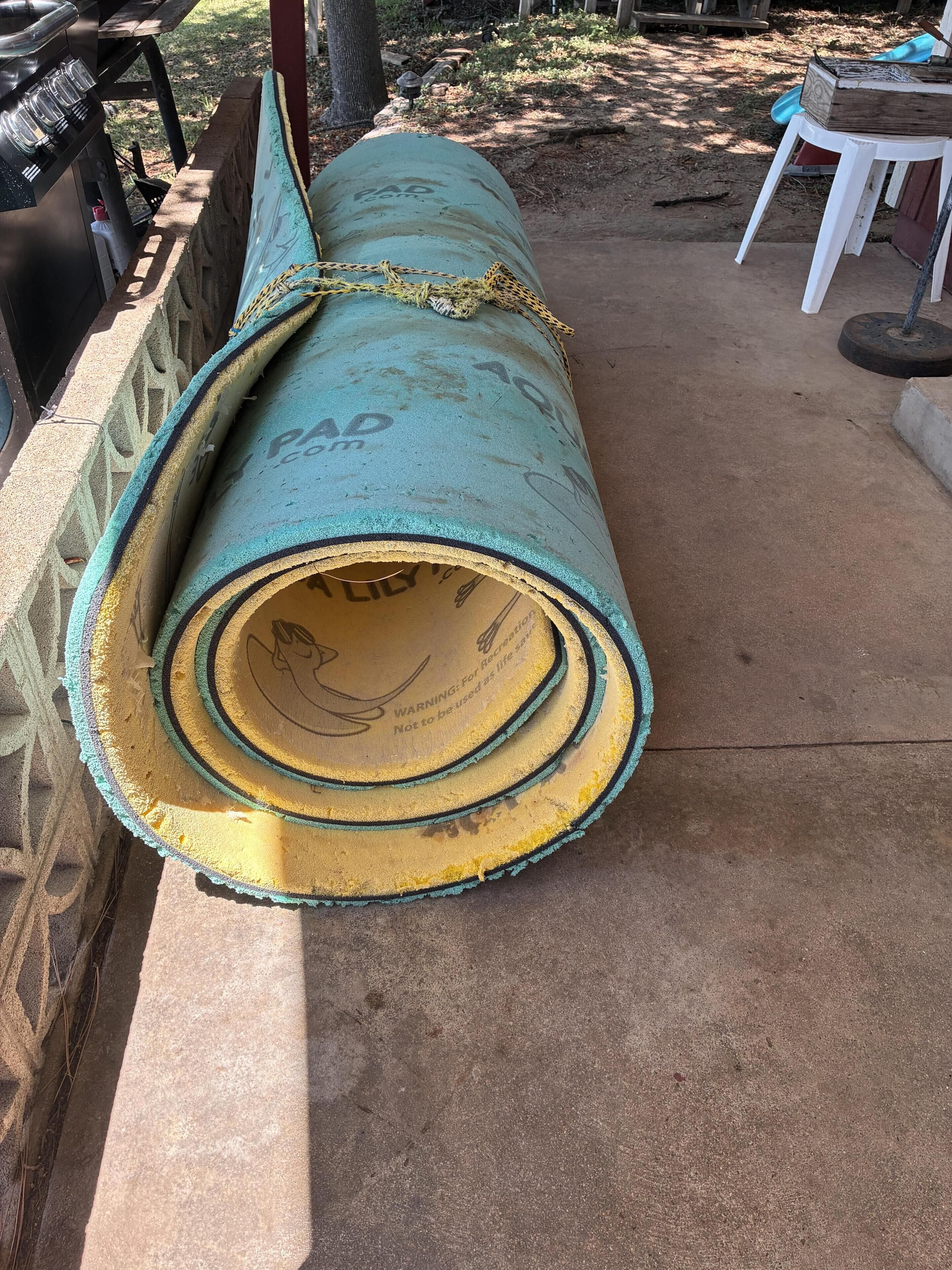A rolled-up mat with a warning label, placed on a concrete surface outdoors.