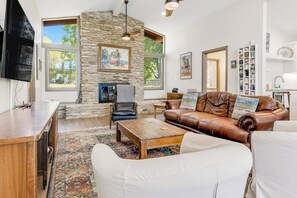 A living room with a stone wall, a fireplace, a leather sofa, a white couch, a coffee table, and a television. - Multiple, Dog-friendly Waterfront Homes With Lake LBJ Views - Snowbird-friendly (Kingsland)