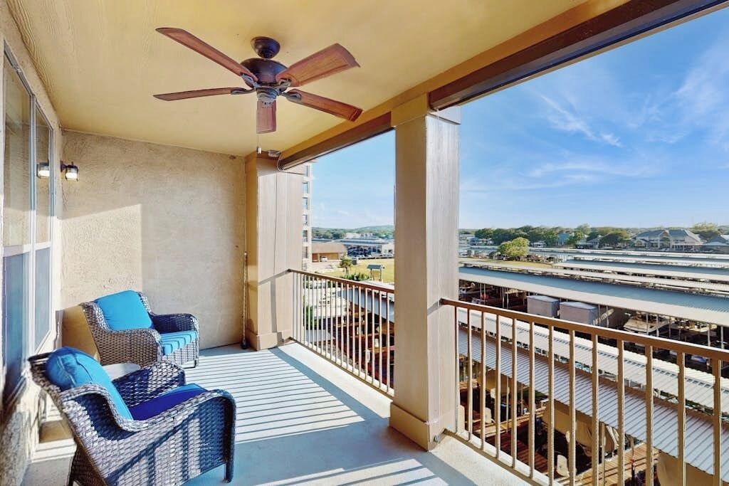 A balcony with wicker furniture, a ceiling fan, and a view of a river and buildings.