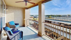 A balcony with wicker furniture, a ceiling fan, and a view of a river and buildings. - Waterfront Condo With Furnished Balcony, Central AC, & Washer/dryer (Horseshoe Bay)