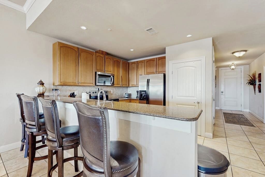 A kitchen with wooden cabinets, a stainless steel refrigerator, a microwave, and a granite countertop.