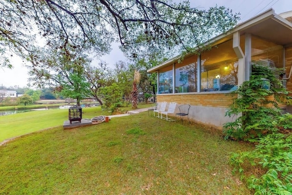 Ein modernes Haus mit überdachter Terrasse, einem Rasen und einem Teich im Hintergrund.