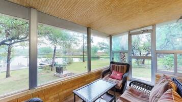 A covered patio with wicker furniture, large windows, and a view of a garden.