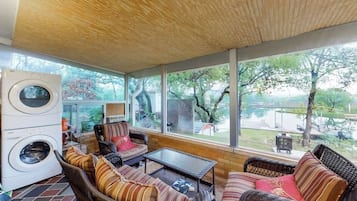 A sunroom with wicker furniture, a washing machine, and large windows overlooking a yard.
