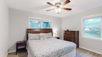 A bedroom with a bed, a nightstand, a dresser, a ceiling fan, and two windows.