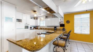 A kitchen with white cabinets, a granite countertop, and a bar area with stools.