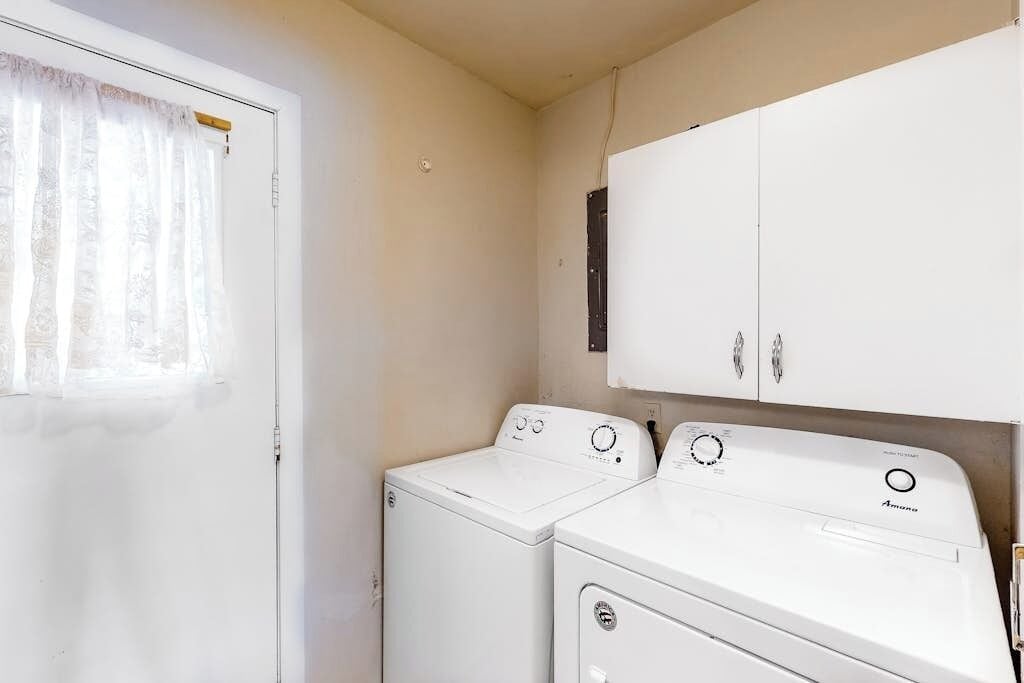 A laundry room with two white washing machines, a white cabinet, and a door with a window.