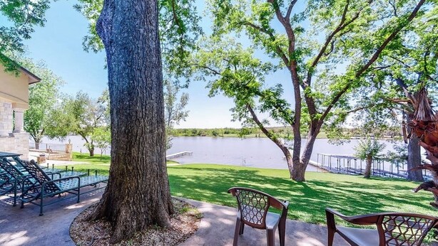 Eine von Bäumen gesäumte Terrasse mit einer Bank, Blick auf einen See und einem Gebäude im Hintergrund.